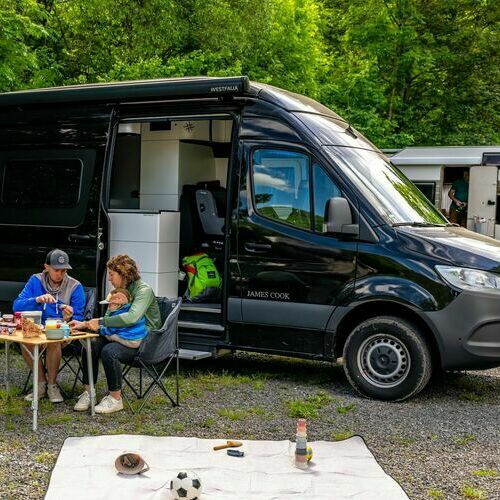 Ein Paar mit Kind sitzt vor seinem Camper. Im Hintergrund ist ein weiterer Camper zu sehen