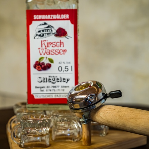 Schnapsgläser auf einem Brett mit Radklingel im Hintergrund eine Flasche Kirschwasser  - 